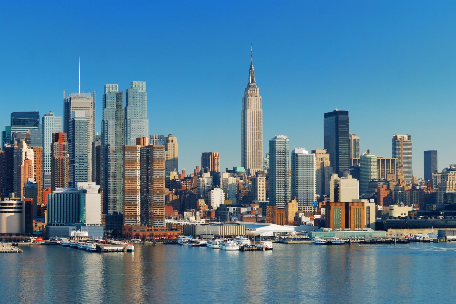 Manhattan Skyline with Empire State Building, New York City over Hudson River with boat and pier.